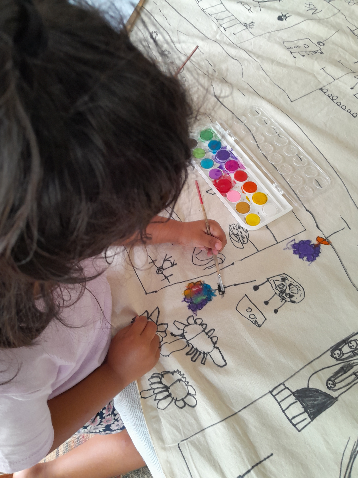 A child painting over a large collaborative drawing filled with imaginative symbols and paths