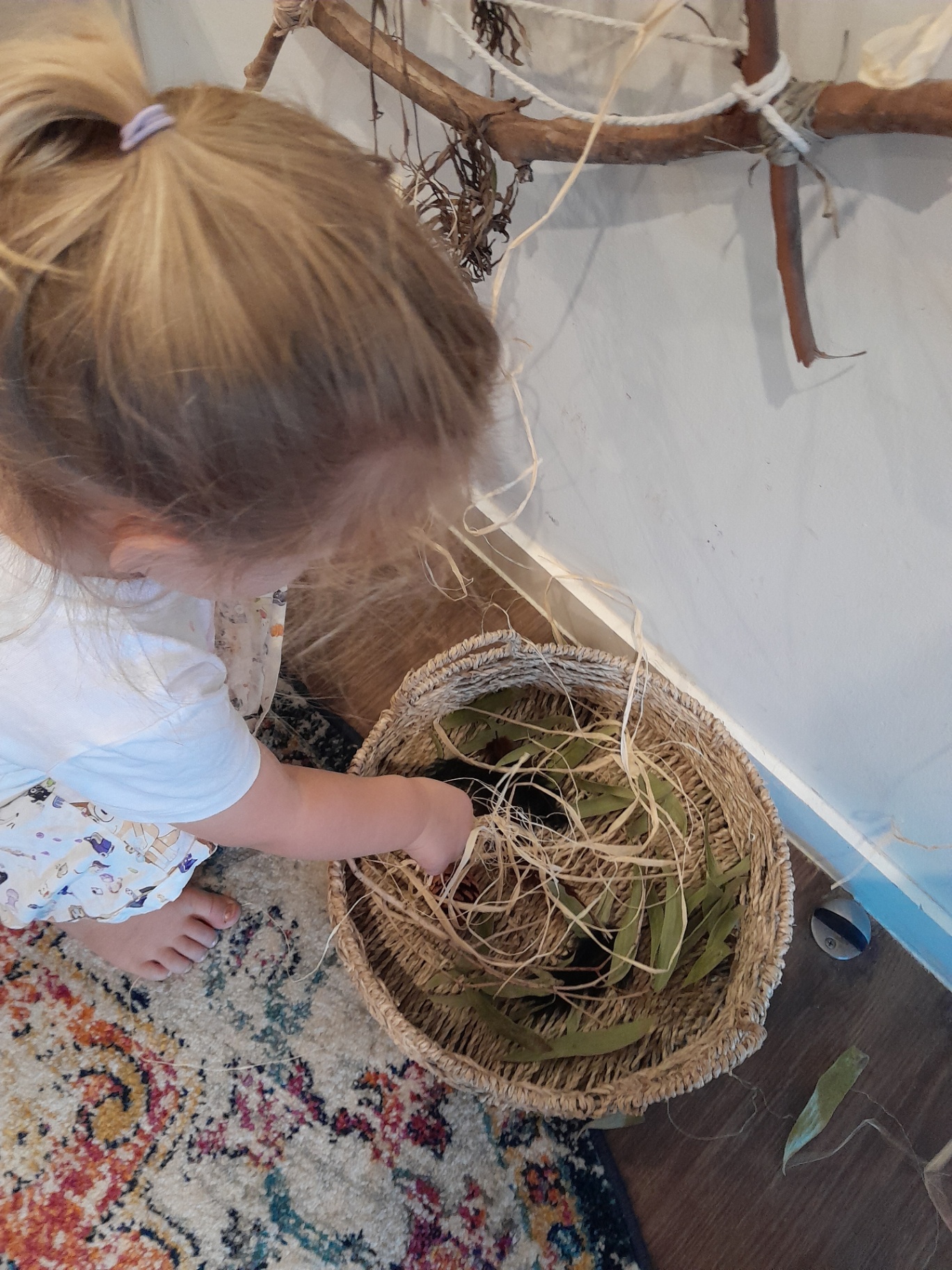A child gathering eucalyptus leaves and raffia from a woven basket