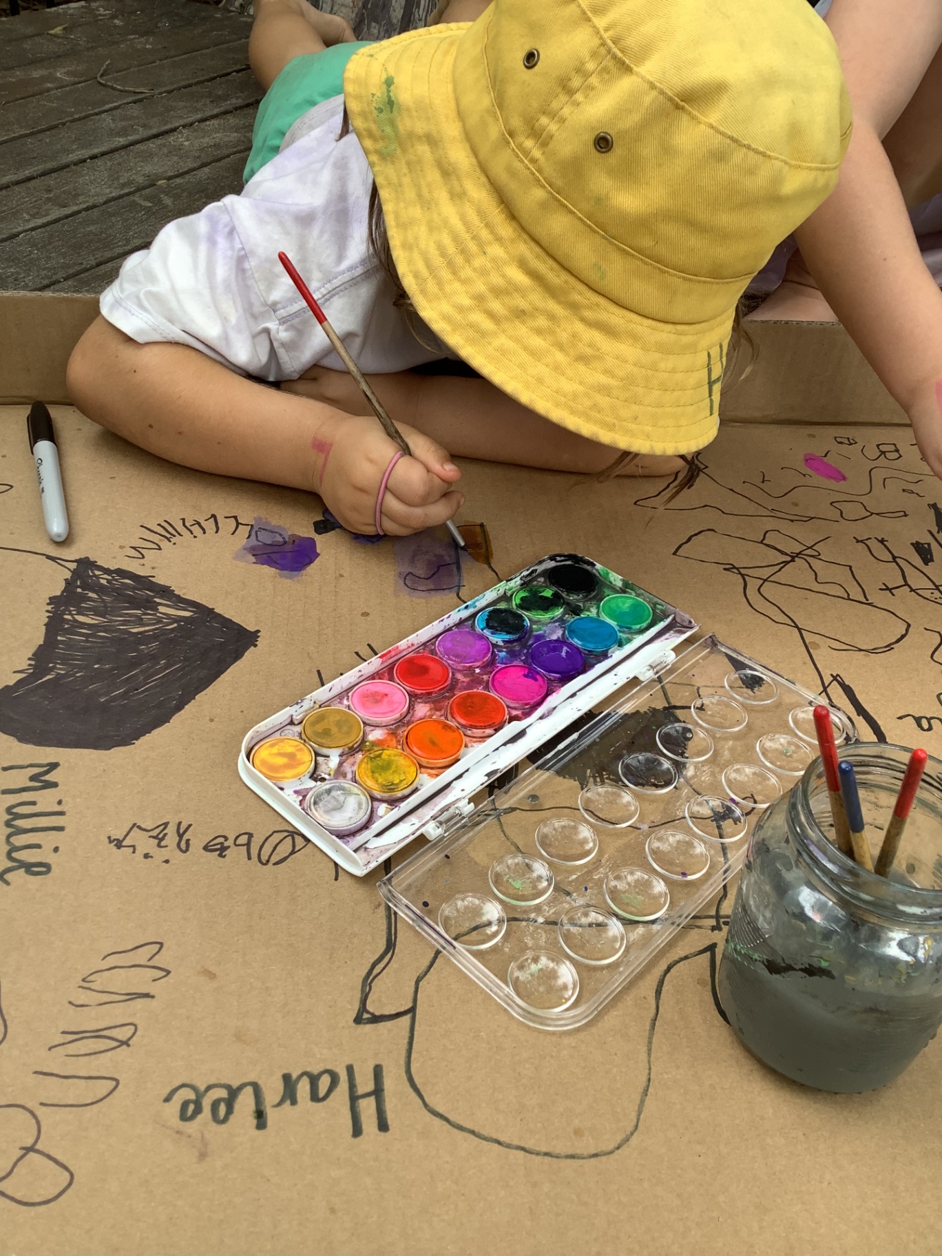 A child painting with watercolours on a large cardboard surface
