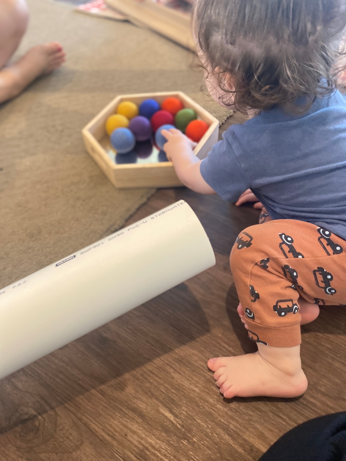 A toddler exploring rainbow felt balls in a wooden tray